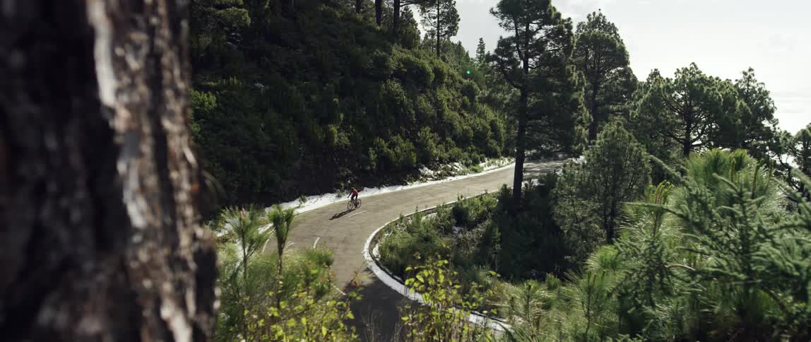 super wide shot of a Cyclist riding up hill through a scenic mountain forest road