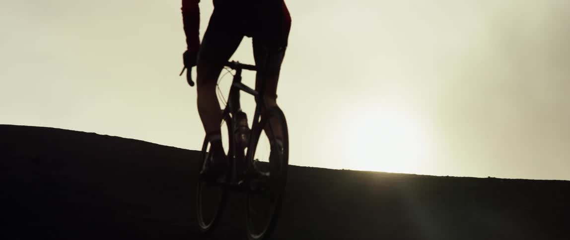 A silhouetted bicyclist riding up a hill in sunset