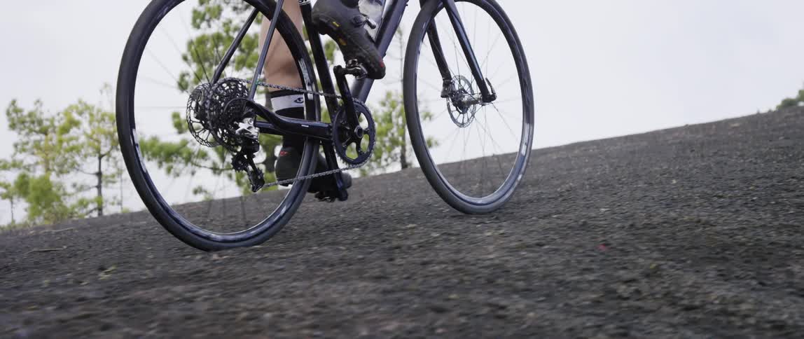 cyclist steering his bicycle uphill through a forest over black gravel