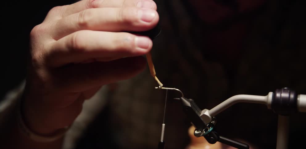 Man dabs fluid onto fishhook held in vise