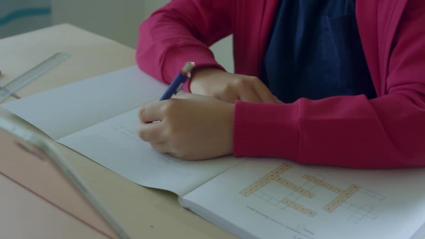 A child sits at a table writing on paper indoors