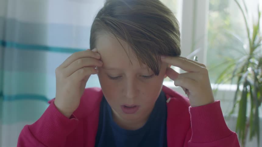 A boy puts his fingers to his temples while doing homework