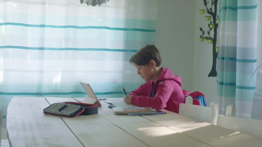 A boy does homework while talking to someone on a tablet