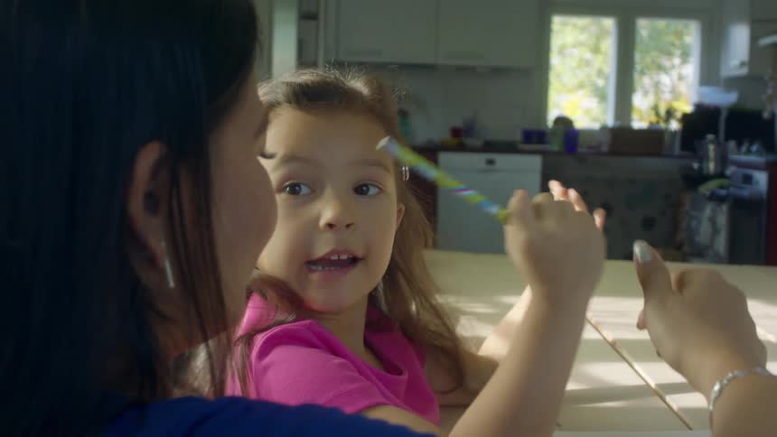 A woman helps her young daughter with homework as they sit at their kitchen table