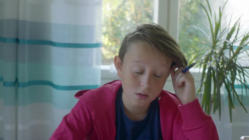 Boy sits at table thinking and studying while viewing tablet