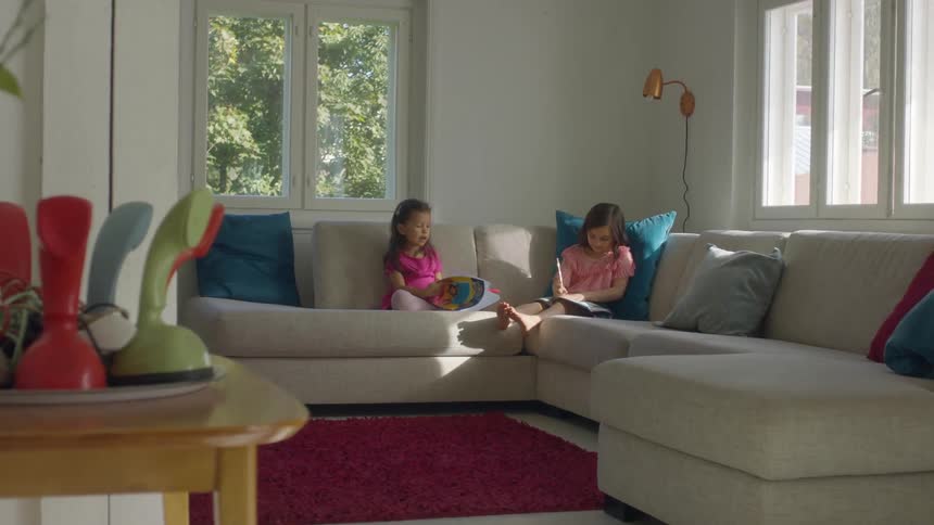 Two girls sit on a couch writing in large books