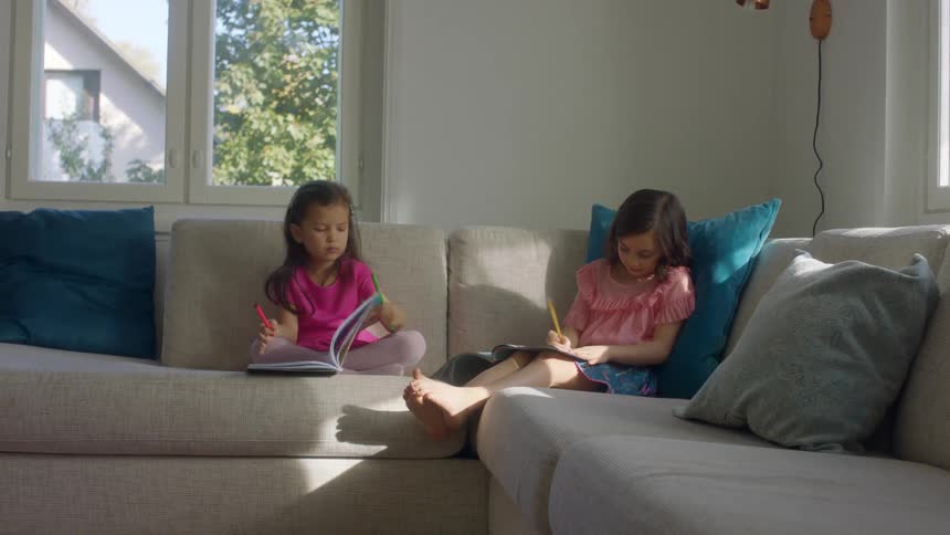 Two young sisters sit on their couch drawing and writing