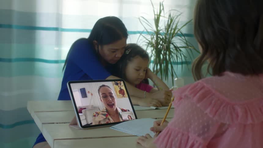 A mother colors with her daughter while her other daughter does school work online with her teacher