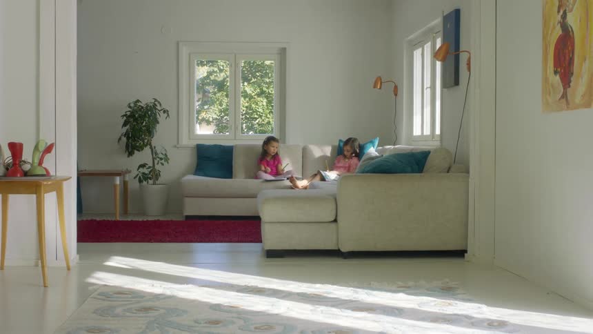 Two sisters sitting on a beige sofa do homework in the living room at home