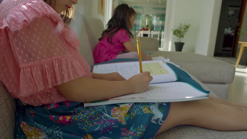 Two young girls work on homework while sitting on a couch