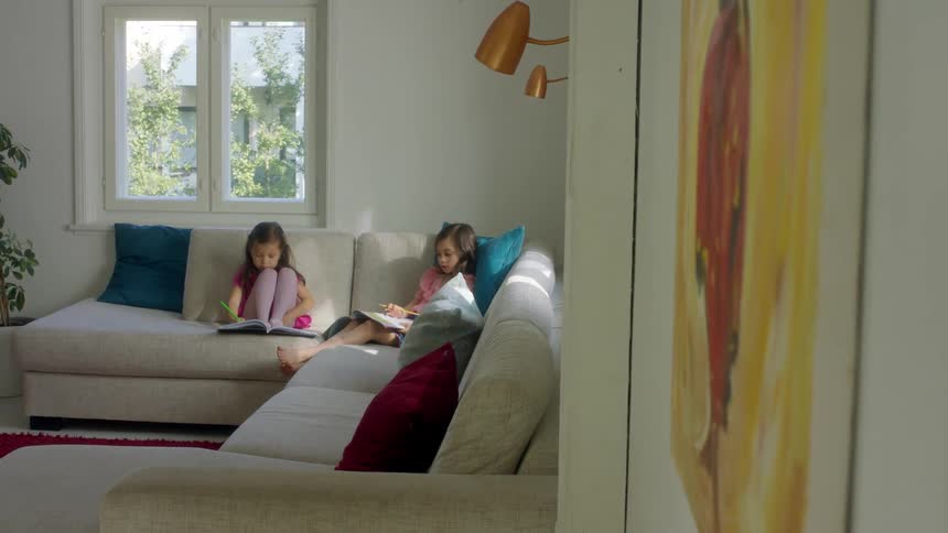 Little girls doing homework together on the couch at home