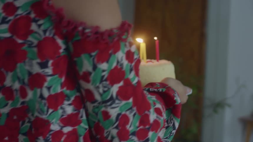 A mother carries a cake with candles through the house and places it in front of a little girl