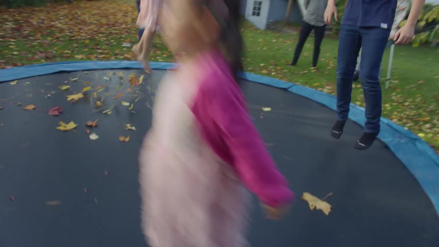 Children jump and play on a large trampoline in their backyard as parents watch