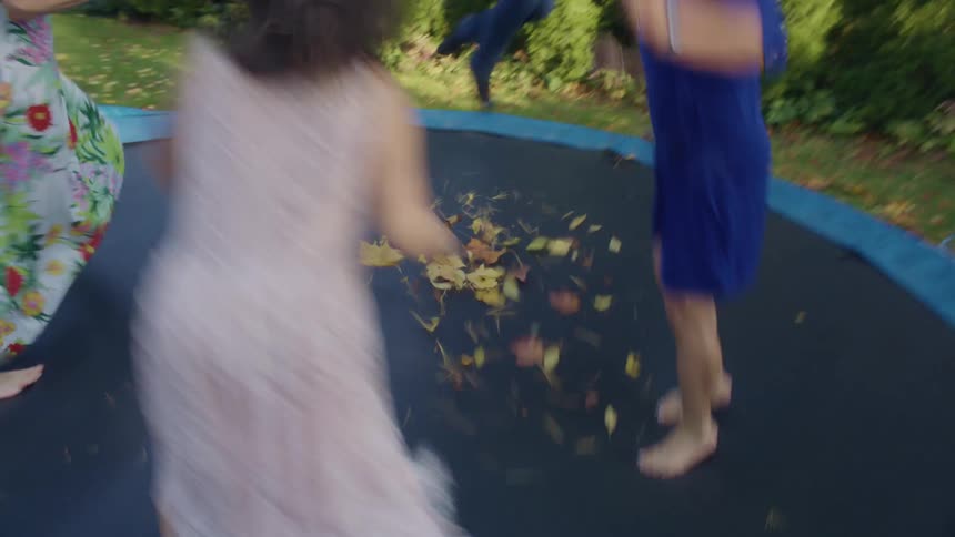 A group of children jump in a circle on a trampoline in the backyard of a house during the day