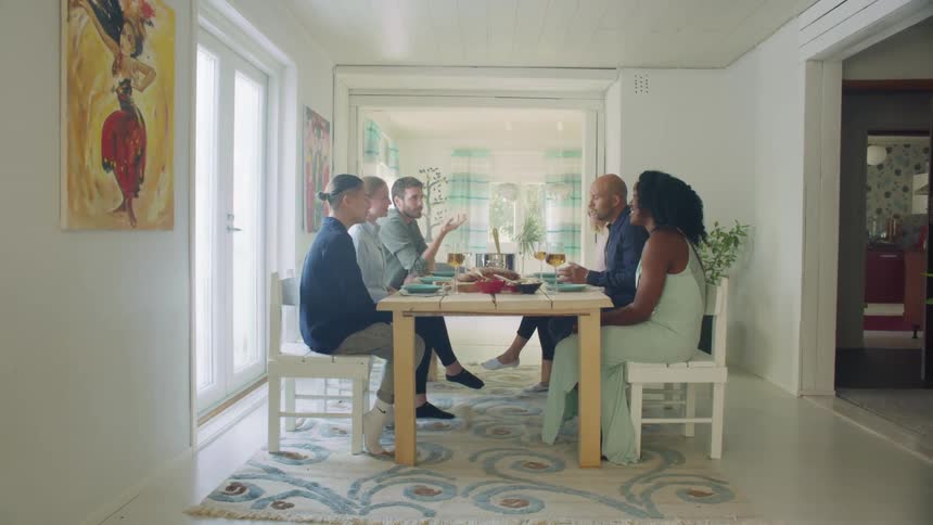A group of people talk as they sit at a table in a home with food and wine