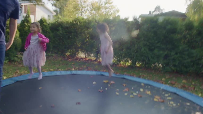 A boy and two girls jumping on a trampoline in the backyard at home near parents