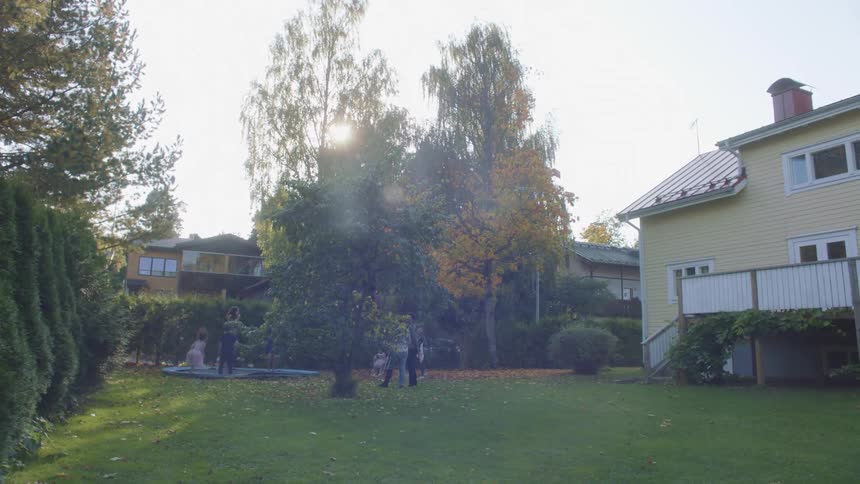 A group of children jump on a trampoline in a back yard as adults watch