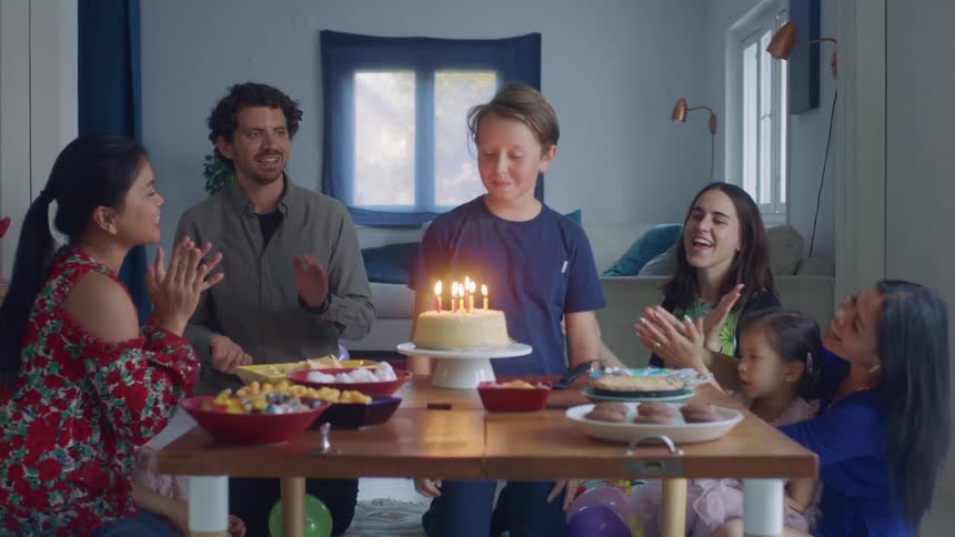 Family and friends sings happy birthday to a young boy at home