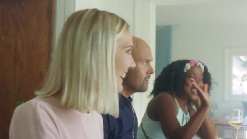 Two women and a man sit at a dining table talking and laughing