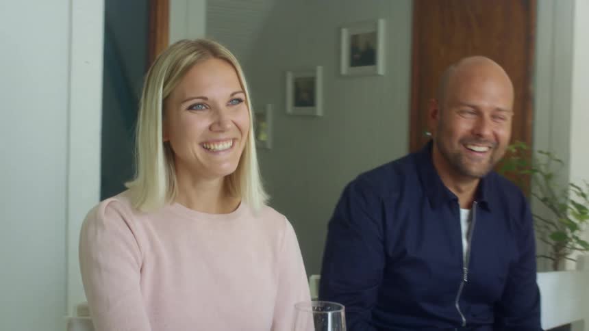 A man and woman gather around a family dinner gathering and laughing at the conversation