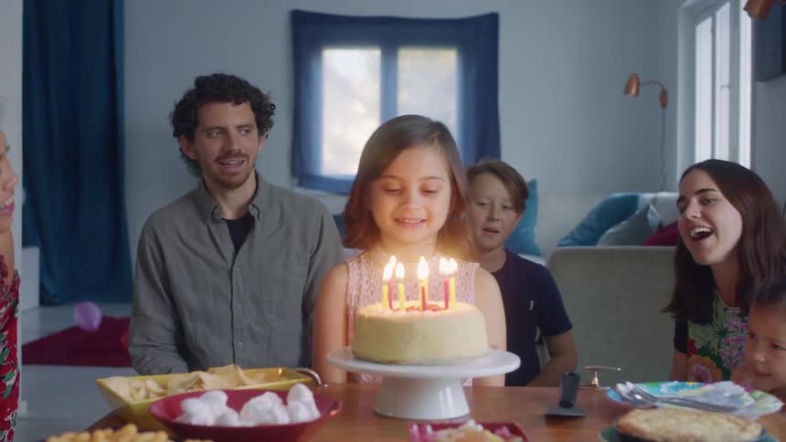 Group of family and friends singing happy birthday to a little girl blowing the candles on a cake