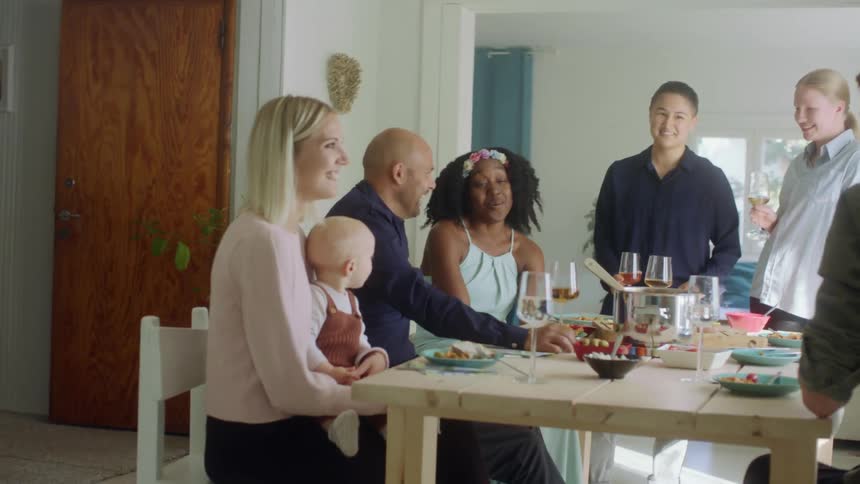 A group of people chat while sitting around a dinner table in a home dining room during the day
