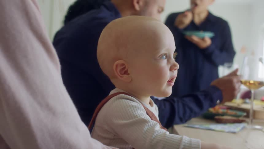 A woman sits at a table with a baby on her lap as others eat a meal