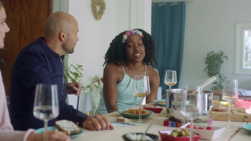 Family and group of friends talking over lunch at home in the dining room
