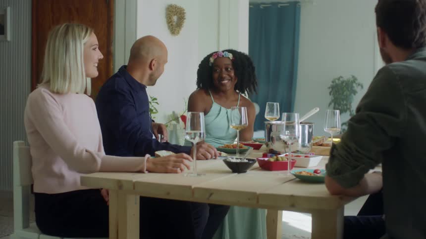 Friends sit around dinner table laughing and talking
