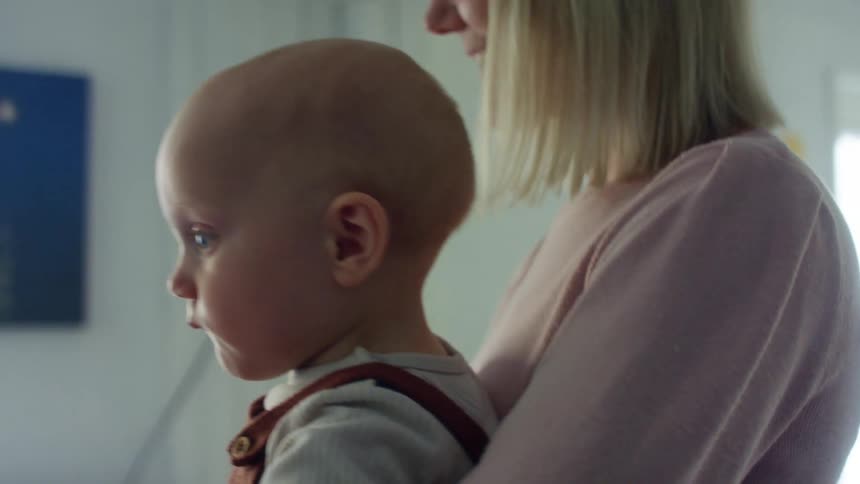 Blonde mother with a pink sweatshirt holds her baby in the living room at home