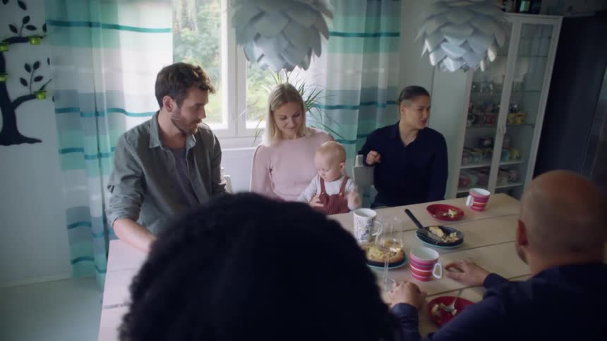 A group of men woman and a baby sit around a dinner table with mugs and dessert