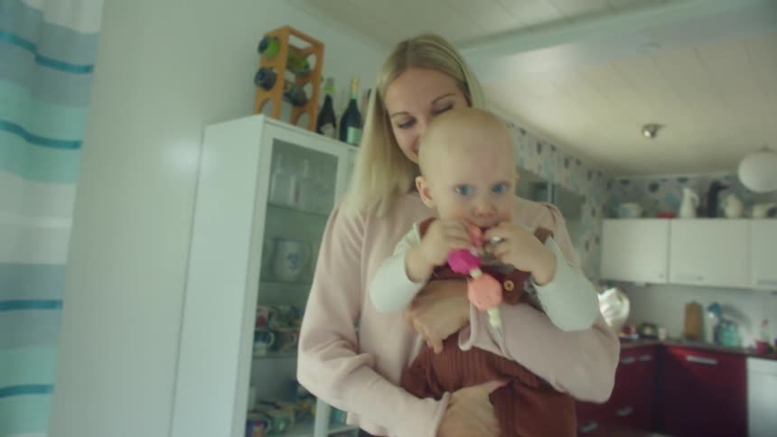 A woman smiles as she holds her daughter and dances around their kitchen