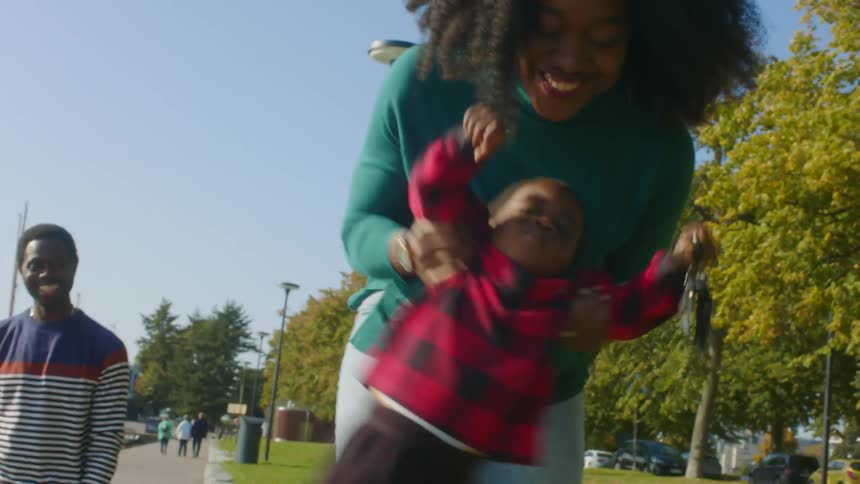 A woman swings her toddler back and forth as they walk through a park