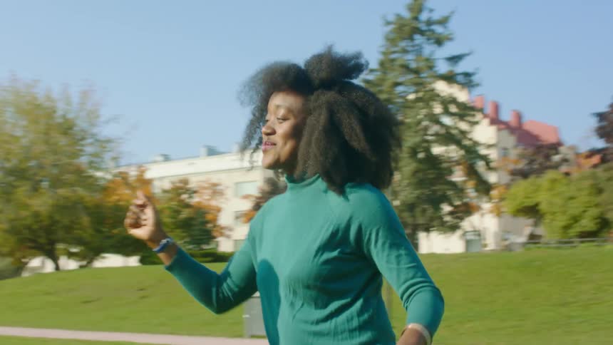 People smile and dance outside on a sunny fall day with tree buildings and grass in the background