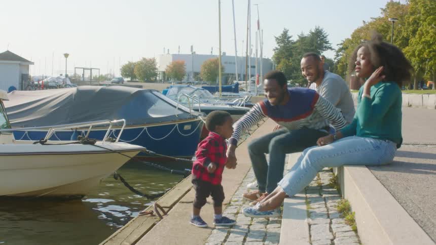 Adults sitting on docks reach out to prevent a toddler from falling into the water