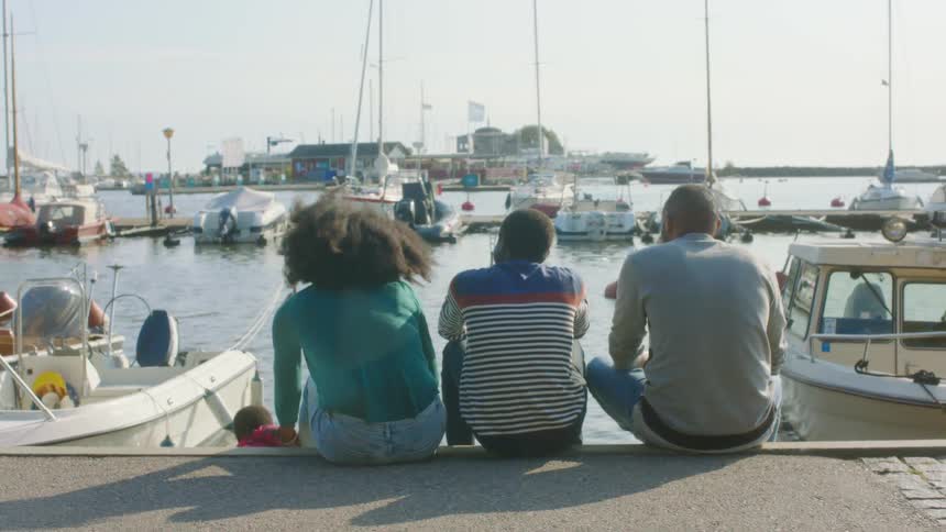 A family sits on the edge of a marina near docked boats