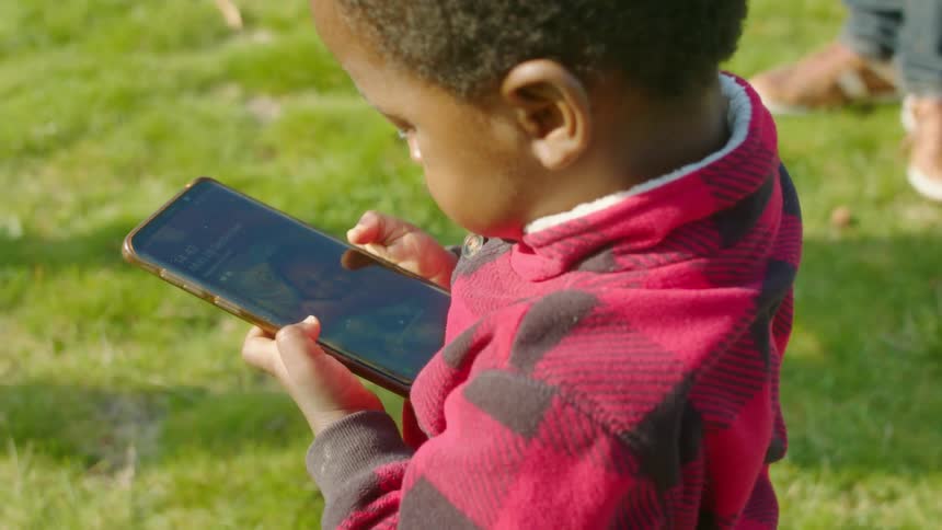 Toddler surrounded by adults using a smartphone over the green grass in the backyard