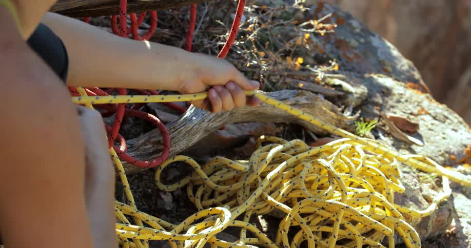 A young woman pulls yellow rope from over the edge of a cliff