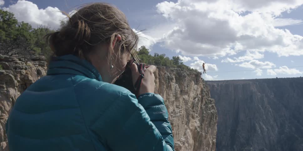 A woman photographs a person tightroping across a canyon