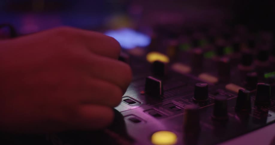 A dj repeatedly moves a switch back and forth while playing in a club under flashing lights