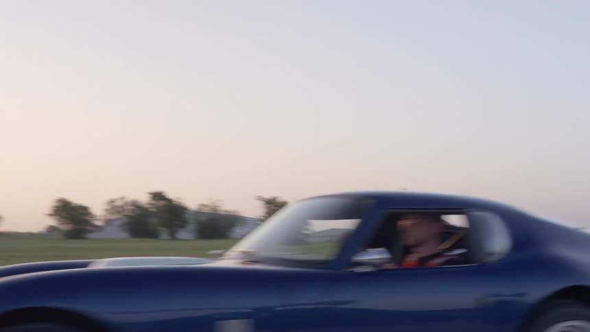 A blue sports car being driven on a rural paved road