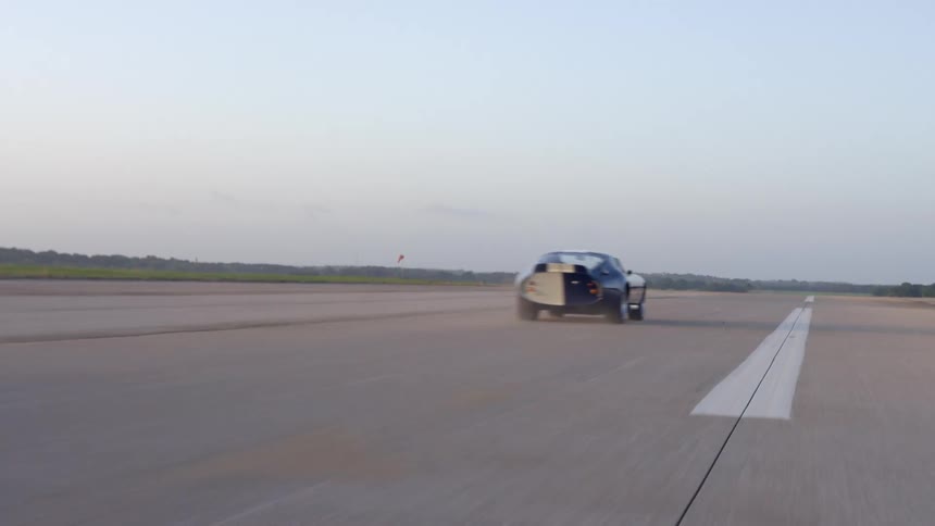 A blue sports car speeding down a paved road in the daytime