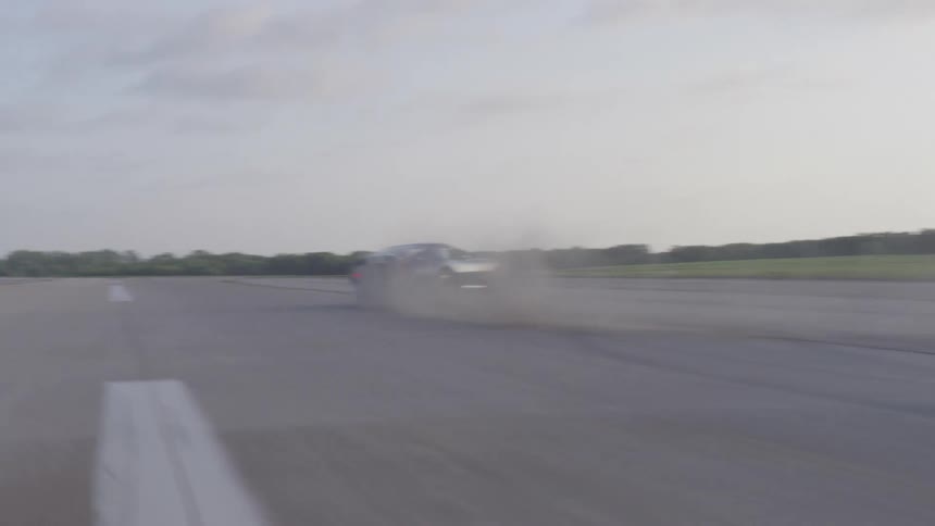 Car drives really fast down otherwise empty road burning the tires creating smoke and turning around quickly