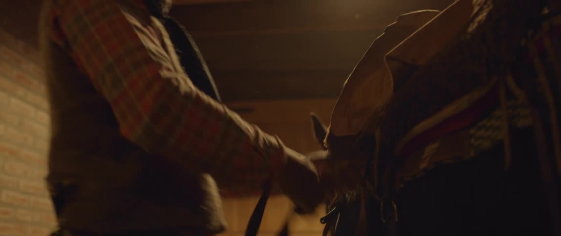A man in a stable tightens a saddle on a horse