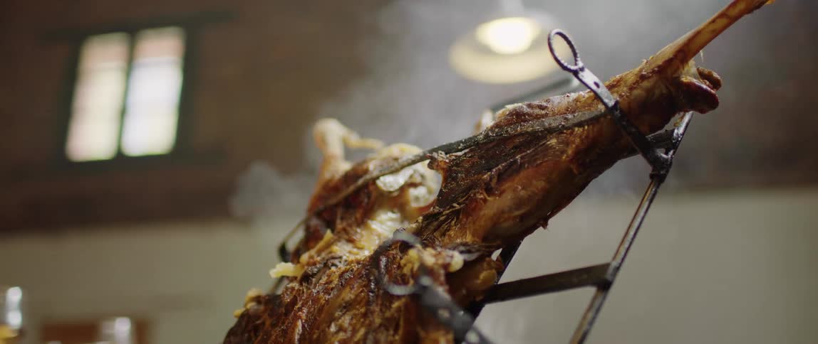 A whole pork roast smoking over fire inside a building