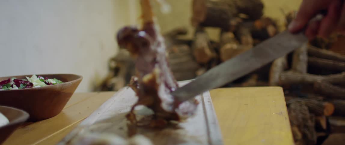 A person uses a large knife to cut the meat off of a turkey leg