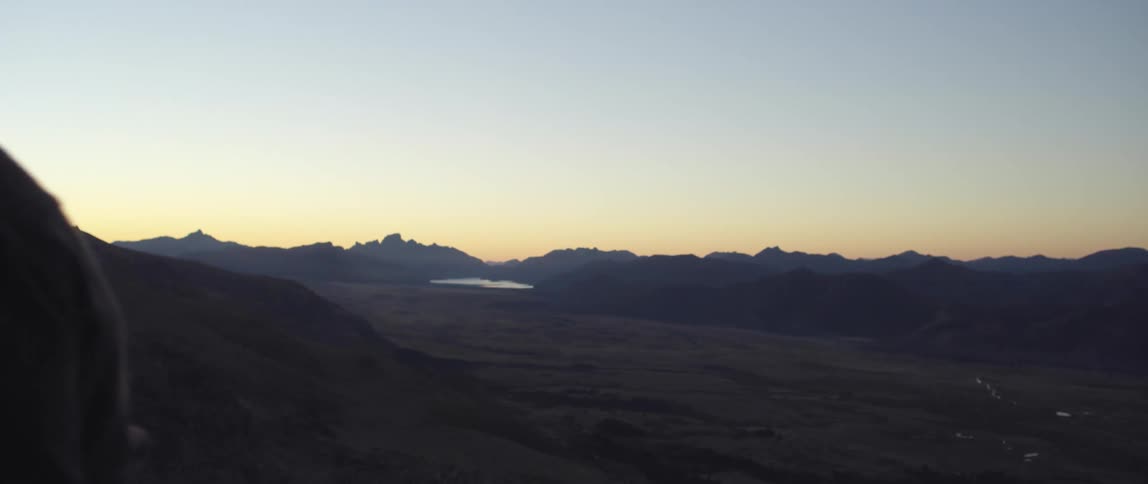 A silhouetted cowboy walking in front of a mountain landscape at dusk