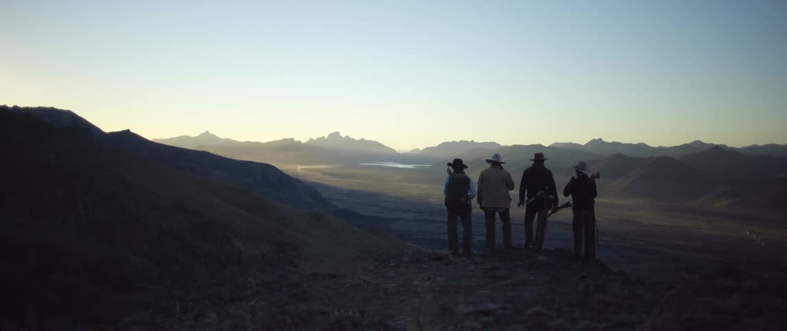 Four cowboys looking at a mountain range at dawn