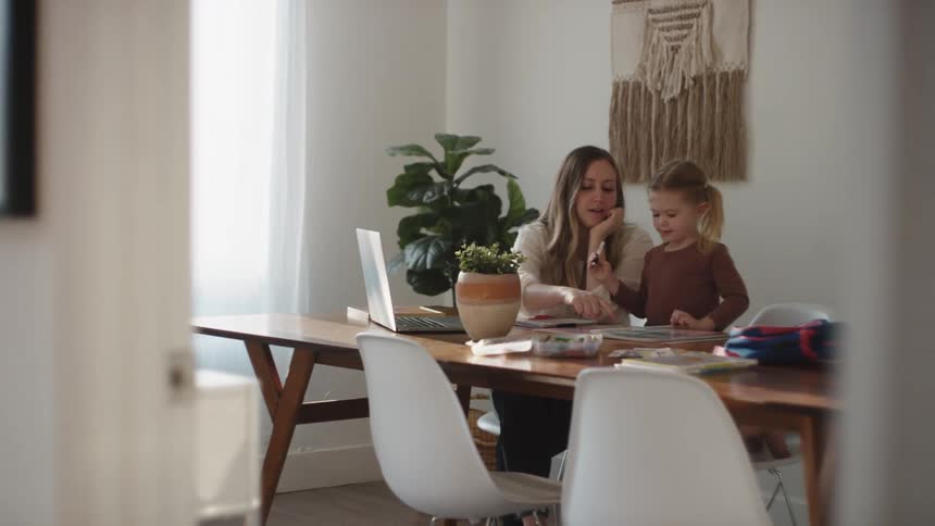 Mother sitting at a table in a living room with her daughter helping her with school work