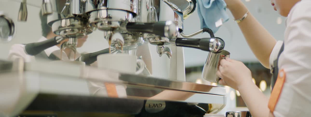 An employee at a coffeehouse steams milk for a drink
